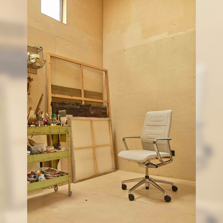 A white Senator Qdos mesh chair with a polished chrome base, shown in a minimalist artist's studio